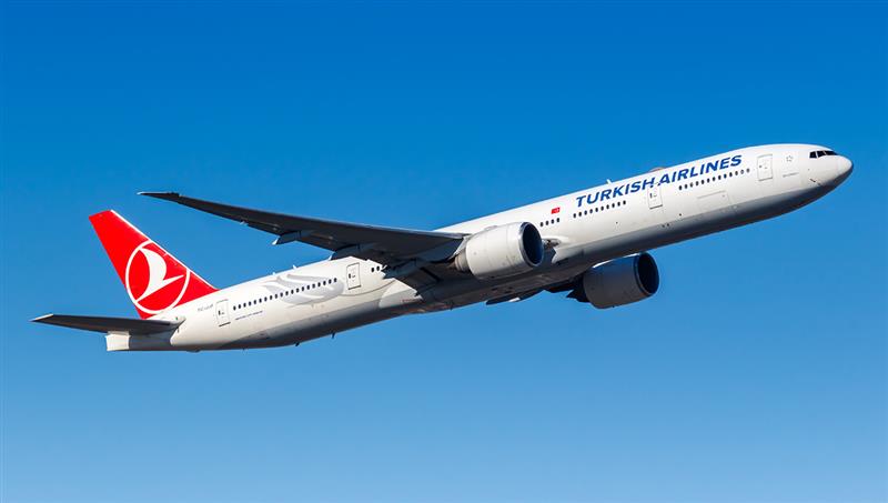 A Turkish Airlines Boeing 777-300ER, painted white with the airline's red logo on the tail, is shown during takeoff against a clear blue sky. As a major intercontinental carrier, this airline is relevant to the search query: what airlines fly to the Philippines?