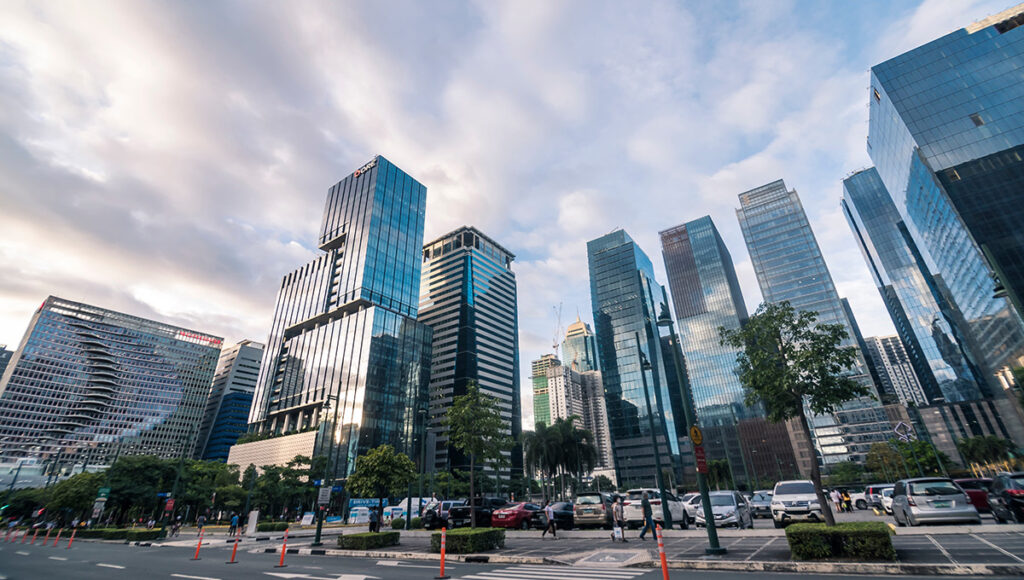 Low-angle view of ultra-modern, glass skyscrapers in Bonifacio Global City (BGC), Taguig, one of the premier business and lifestyle districts in the Metro Manila area. The clean, well-lit street and modern design contribute to the perception of a safe and secure area when asking, is Manila safe?