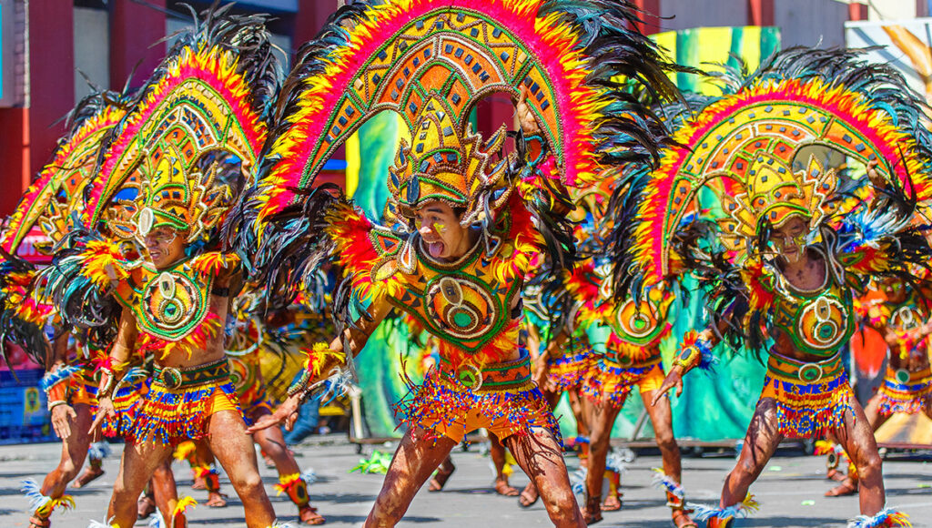Performers in elaborate, colourful feathered costumes and headdresses dancing in a street parade at the Dinagyang Festival.