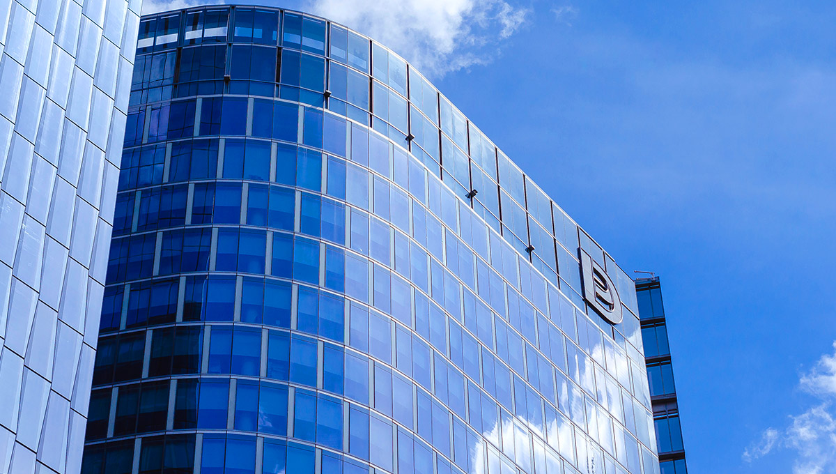 A modern, curved blue glass skyscraper in a financial district under a bright blue sky, reflecting clouds, showcasing the contemporary side of the city and suggesting that is Manila worth visiting.