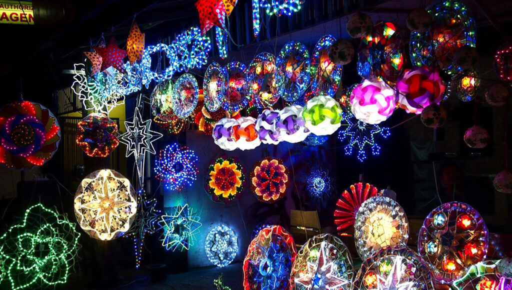 A vivid nighttime display of large, brightly illuminated Parol lanterns and other Christmas lights, including a Nativity scene, symbolises a key element of Filipino Christmas traditions.
