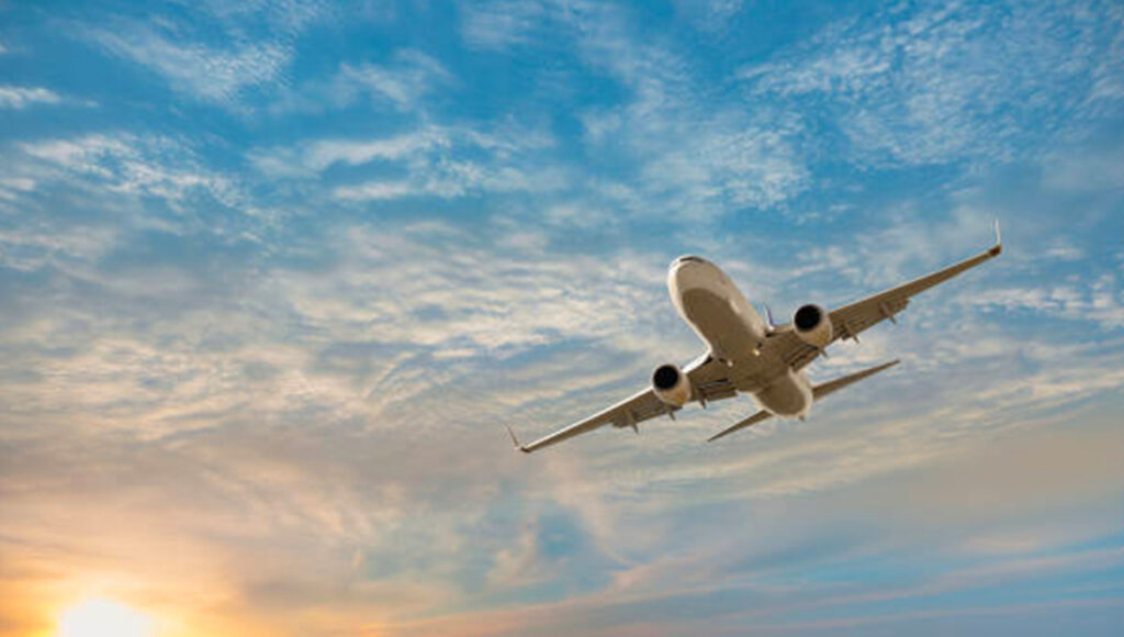Passenger airplane flying over turquoise tropical waters at sunset, illustrating comfort and convenience for travelers using direct flights to Philippines from UK.