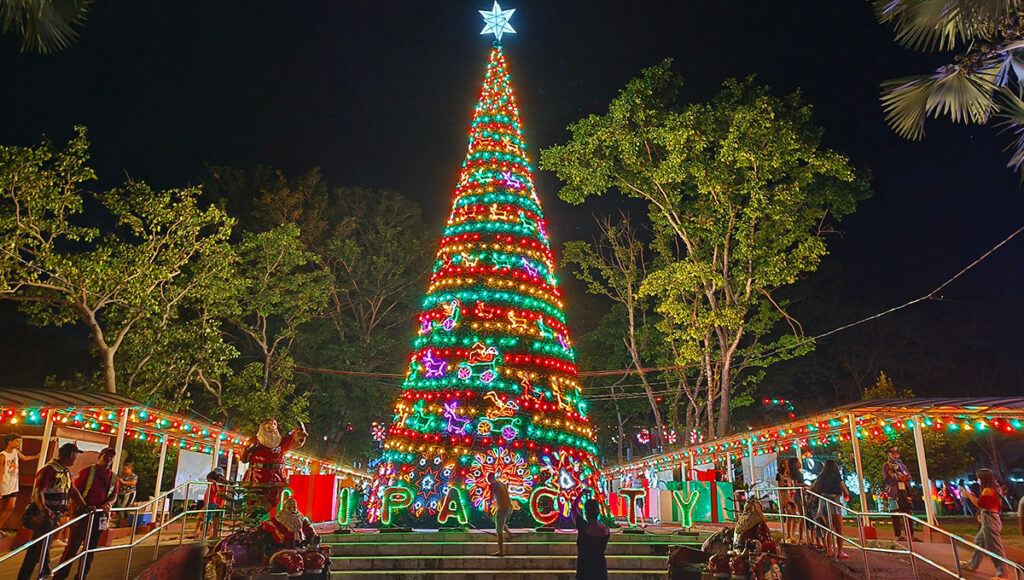 A magnificent, brightly lit Christmas tree adorned with colourful lights and a shining star, illuminating a public square at night in the Philippines. This festive scene is a perfect visual for illustrating fun facts about the Philippines' incredibly long and joyous Christmas season, which famously begins in September.