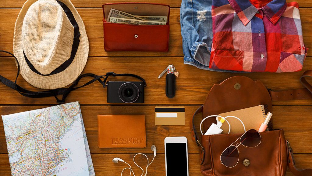 A flat lay of travel essentials packed on a wooden surface, including a hat, a map, a camera, a passport, a wallet with cash, credit cards, a smartphone, and a change of clothes, emphasising preparation and making it clear is Manila worth visiting.
