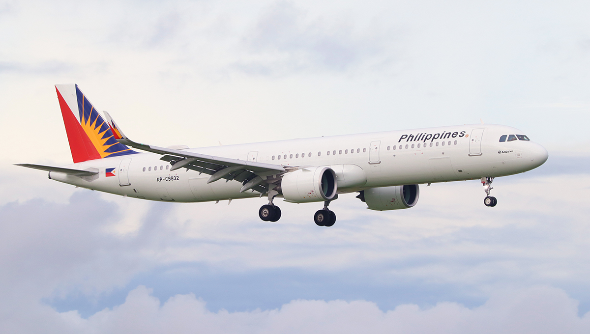 A Philippine Airlines (PAL) Airbus A321 aircraft is pictured banking slightly against a cloudy sky, showcasing the carrier's prominent sun logo on the tail. As the Philippines' national flag carrier, this airline is a primary result when investigating what airlines fly to the Philippines.
