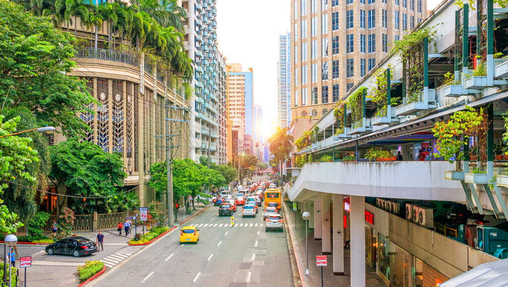 Wide, well-maintained street in Makati City, Metro Manila, flanked by lush tropical trees and upscale commercial buildings. This organized cityscape reflects the well-developed and secure nature of the area, providing evidence for those asking, is manila safe.