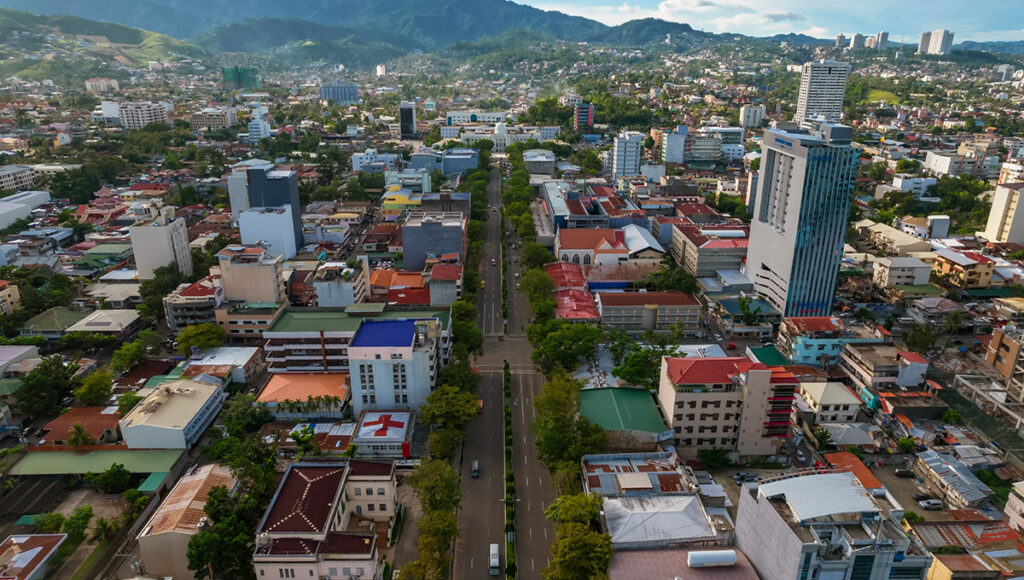 Cebu City Sinulog Festival location: Aerial view of the Cebu City urban landscape showing a major avenue, high-rise buildings, and lush green mountains in the background.