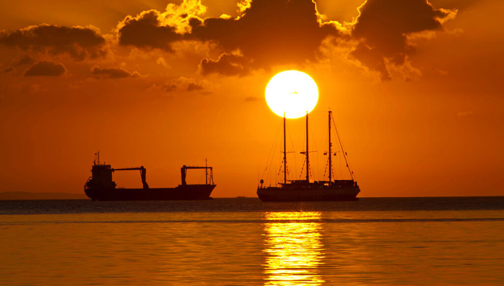 A breathtaking sunset over the water of Manila Bay, featuring a brilliant orange and red sky with a white sun hovering just above the horizon and small boats silhouetted below, showcasing one of the most popular free things to do in Manila.