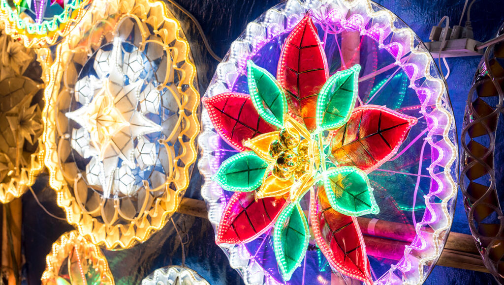 Close-up of bright, illuminated Filipino Christmas lanterns (Parols) from San Fernando, Pampanga, featuring intricate, colorful floral designs and patterns of lights.
