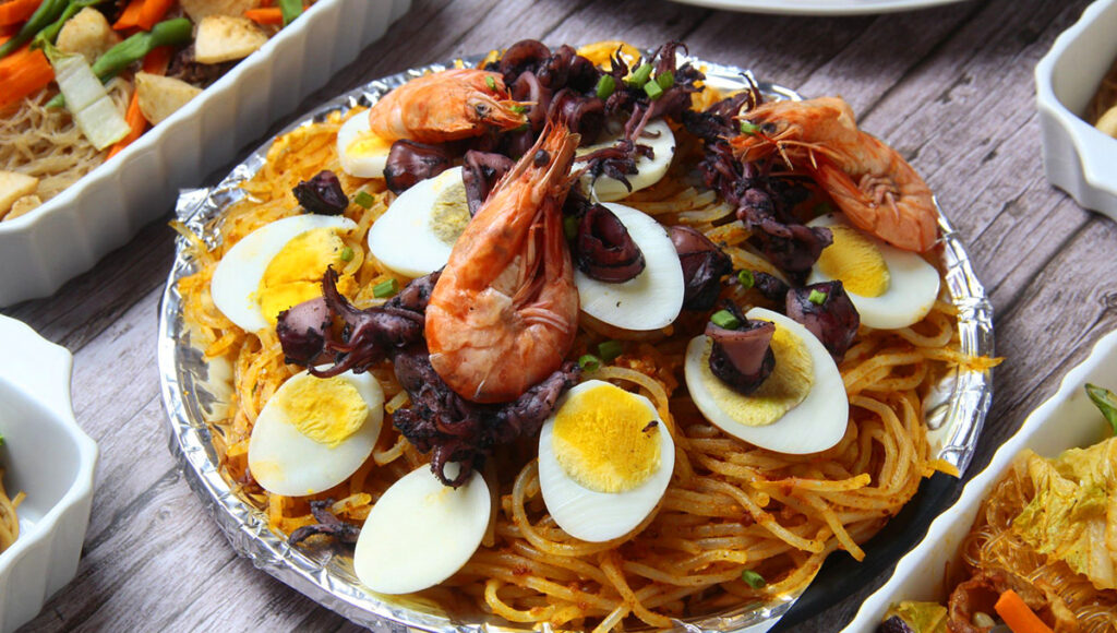 A plate of Pancit Malabon, a classic Filipino Christmas food noodle dish topped with shrimp, eggs, and fish flakes