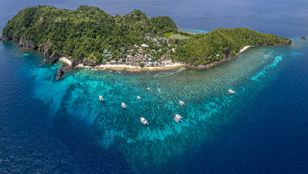 Aerial view of Apo Island village and its protected coral reef area, visible below the boats in the clear blue water. Famous for Philippines scuba diving.