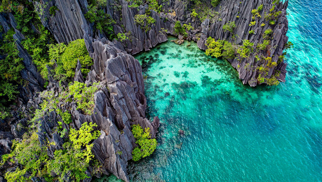 Aerial view of a secluded cove surrounded by jagged limestone cliffs in Coron, Palawan. A hidden gem for Philippines travel.