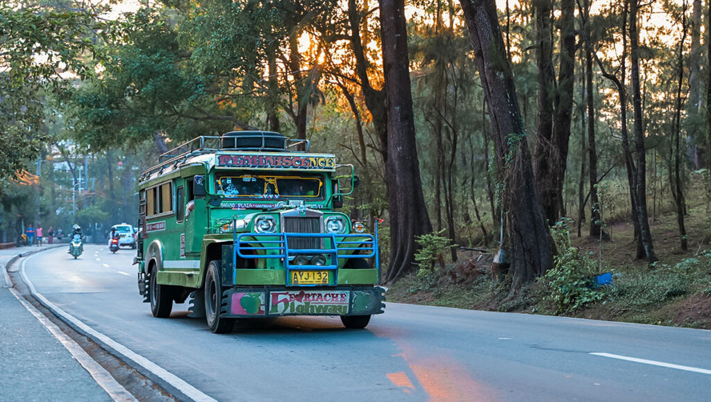 A brightly painted green Jeepney, the iconic and colorful public transportation of the country, driving down a tree-lined road at sunset, symbolizing a unique element of what is Philippines famous for.