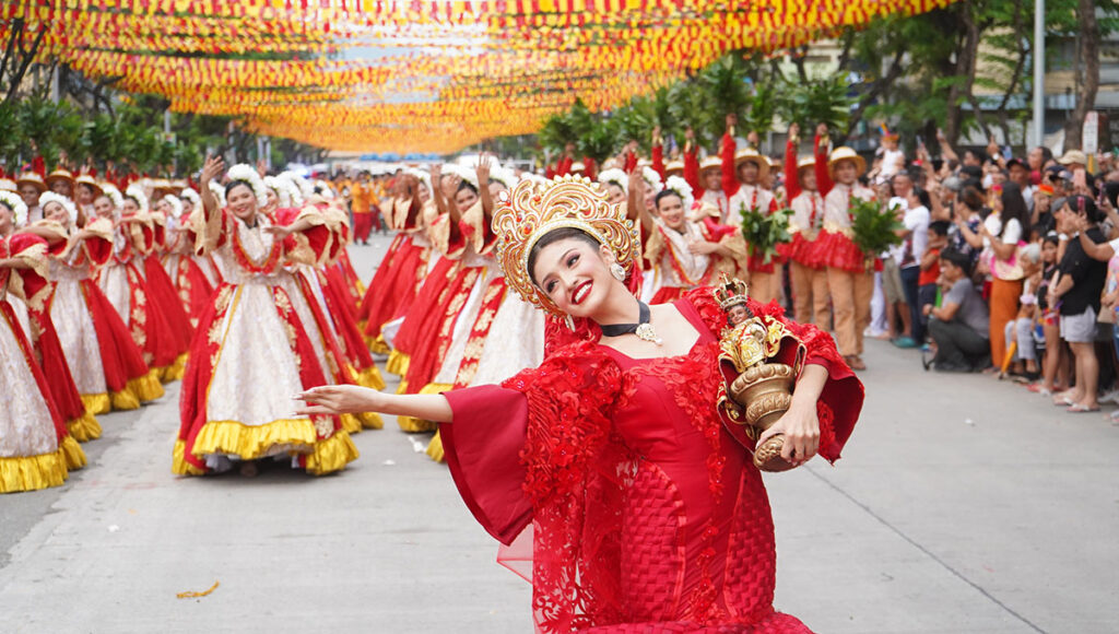Dancers in elaborate red and gold costumes performing a street parade for the Sinulog Festival in Cebu, demonstrating the lively fiesta culture and Catholic traditions that are part of what is Philippines famous for.