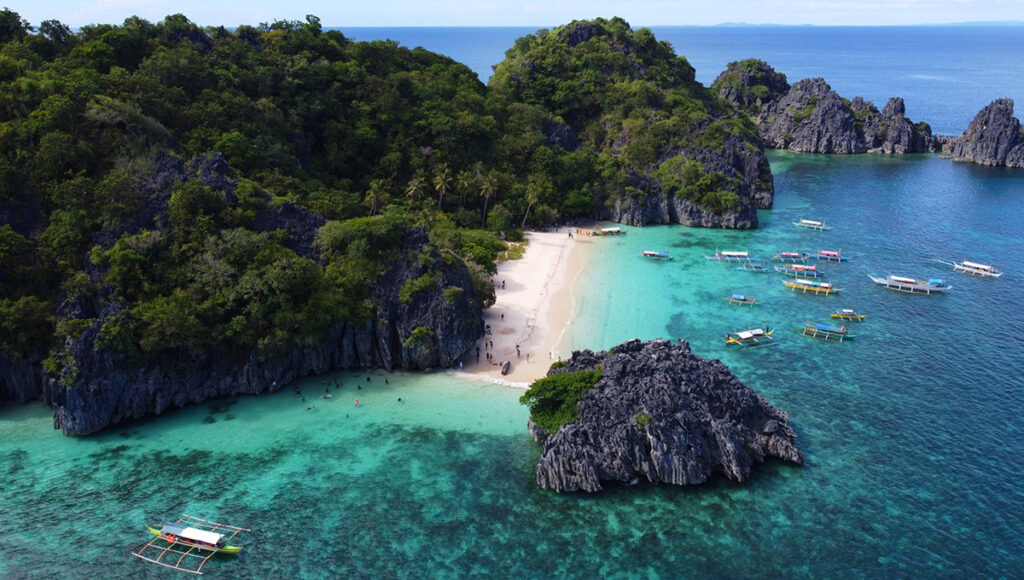 Caramoan Islands beach with towering limestone cliffs and outrigger boats. A popular stop for philippines tours.