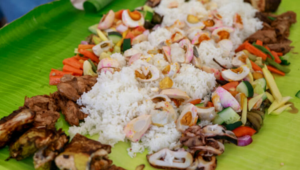 Guests gather around a communal spread with a steaming mound of rice at the center, a classic Boodle Fight Philippines feast with assorted Filipino dishes.