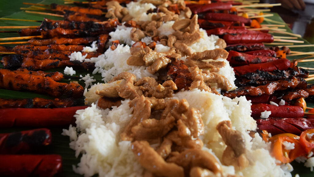 Lechon belly and grilled meats are ready for a communal Boodle Fight Philippines feast on banana leaves.