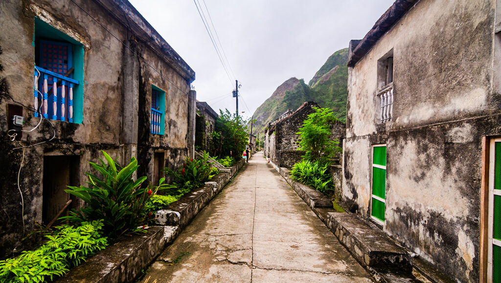 This cultural Batanes tourist attraction features Chavayan Village, known for its traditional Ivatan stone houses built to withstand strong typhoons. The image reflects a quiet coastal community with thick stone walls and rustic architecture, surrounded by nature, giving a strong sense of heritage, resilience, and authentic island life in Batanes.