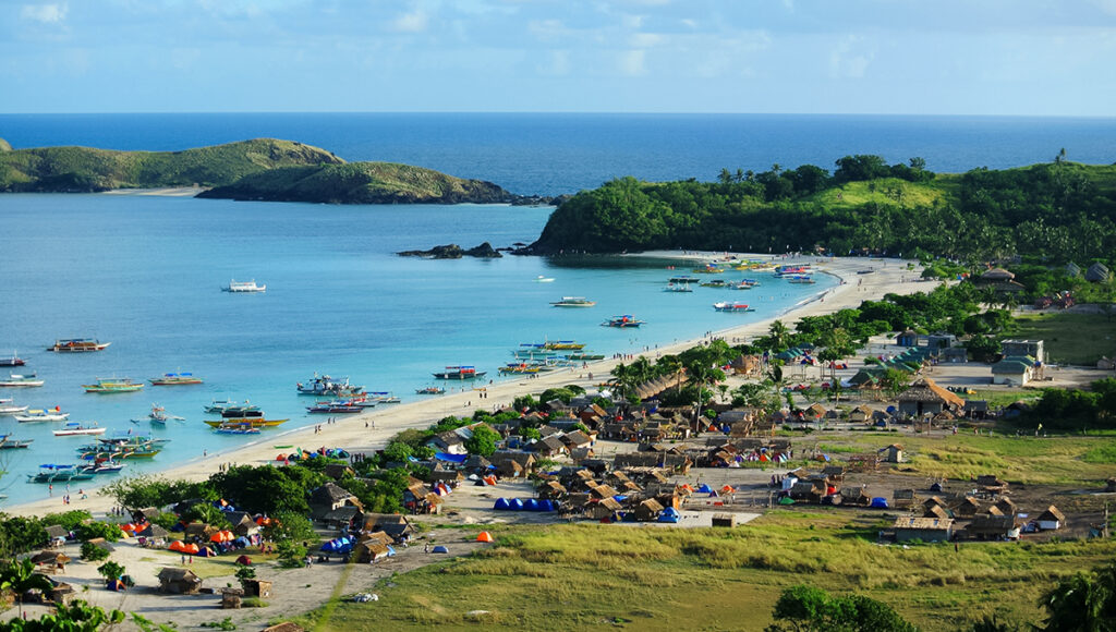 Undiscovered beaches in the Philippines at Calaguas Island with a sweeping crescent shoreline, sapphire waters, and rolling green hills