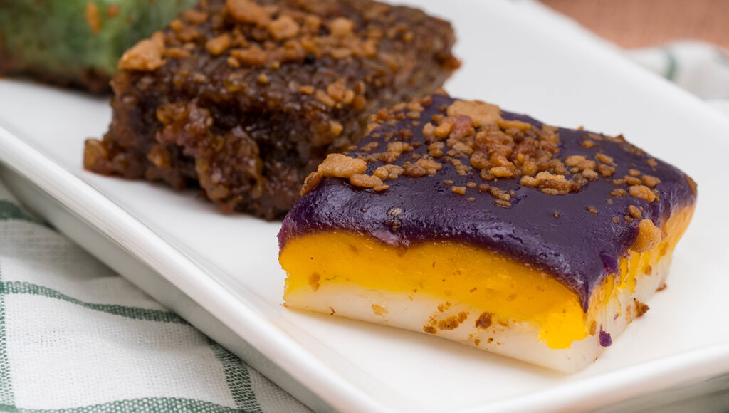 Layered Filipino desserts sapin-sapin in purple, yellow, and white with latik.