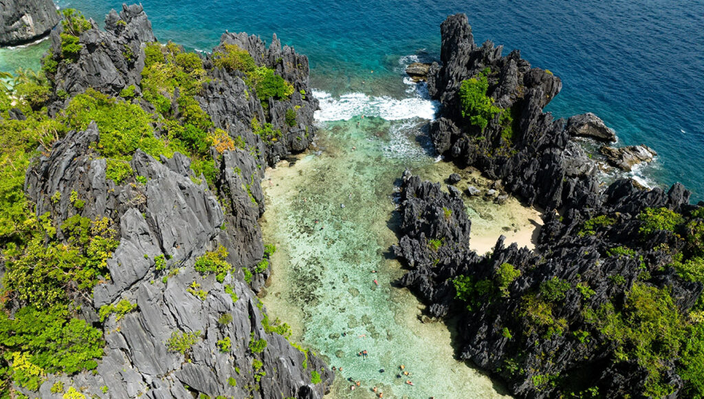 Top-down view of swimmers in a hidden turquoise lagoon surrounded by jagged rocks at one of the Palawan beaches.