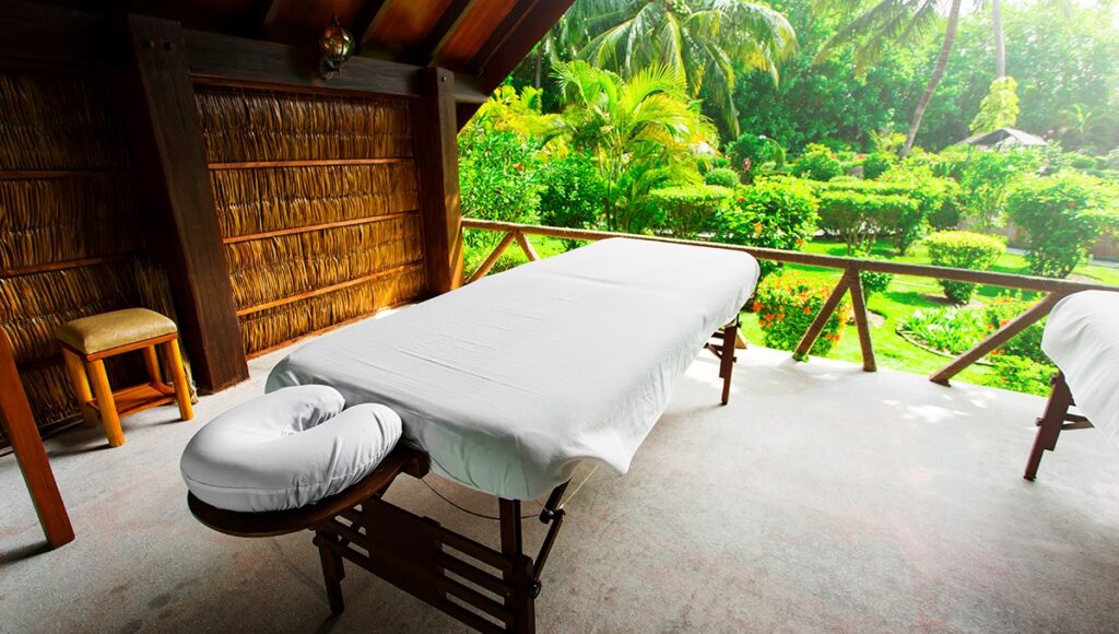 An outdoor spa massage table set on a wooden balcony overlooking a lush tropical garden, offering a glimpse into the wellness services at family resorts in Philippines.