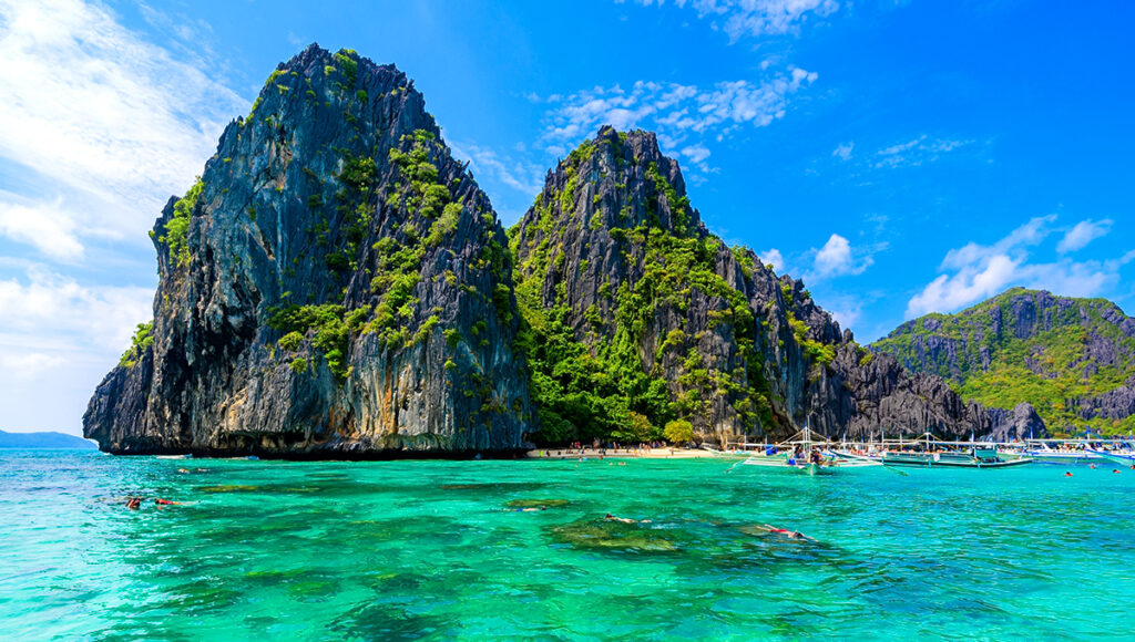 Towering limestone cliffs rising from emerald green waters where tourists swim and boat, a short trip from the primary siargao surf spots.