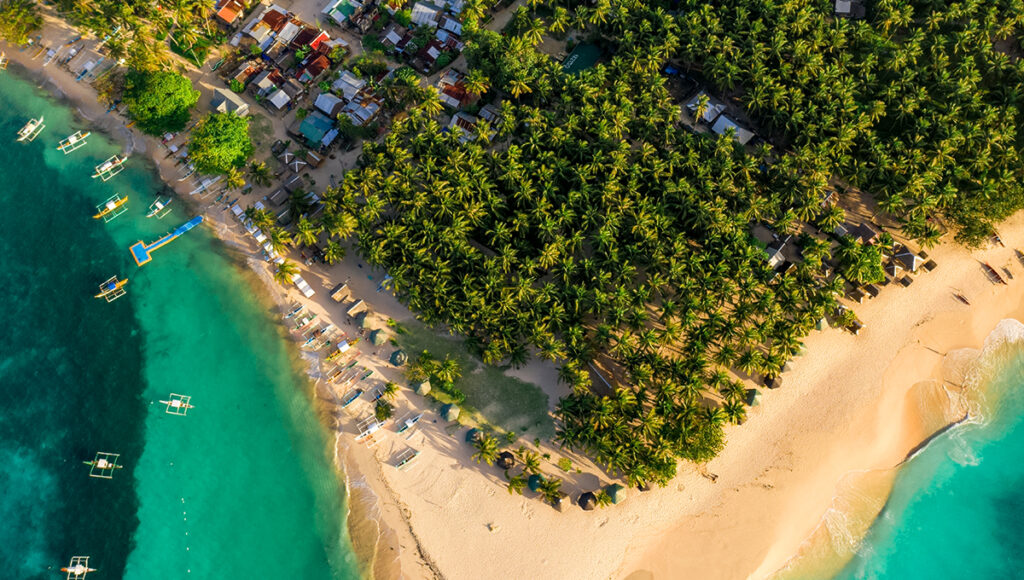 Aerial drone view of the coconut groves and white sand beaches of Daku Island, a must-visit location for those exploring Siargao surf spots.