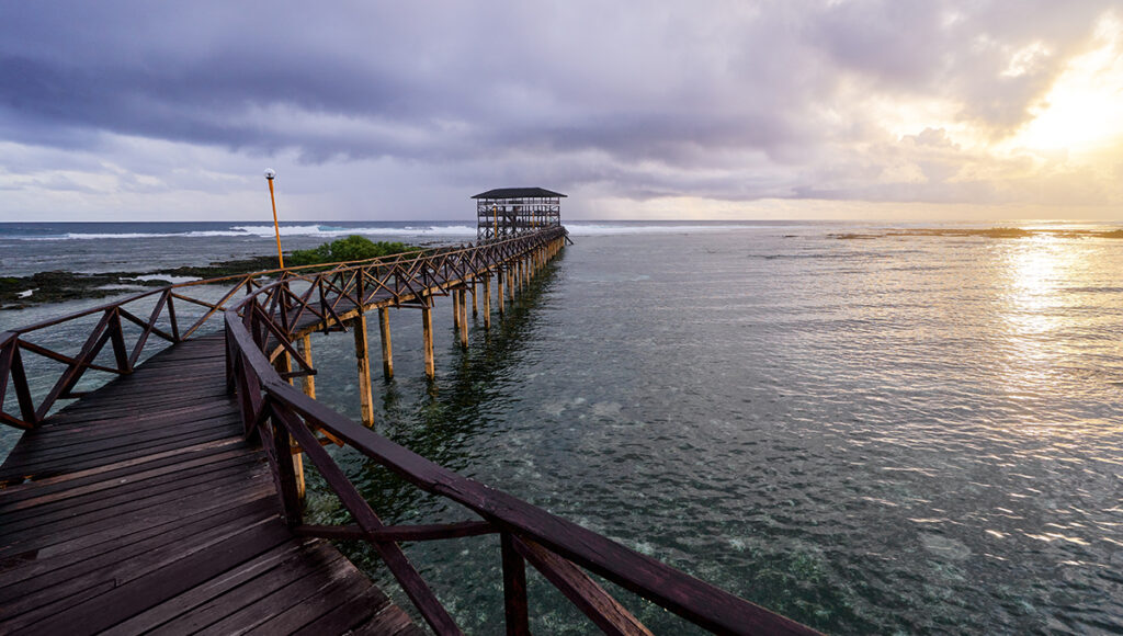 Low-angle sunset shot on a Siargao beach, with the golden sun reflecting off the water's edge and wet sand.