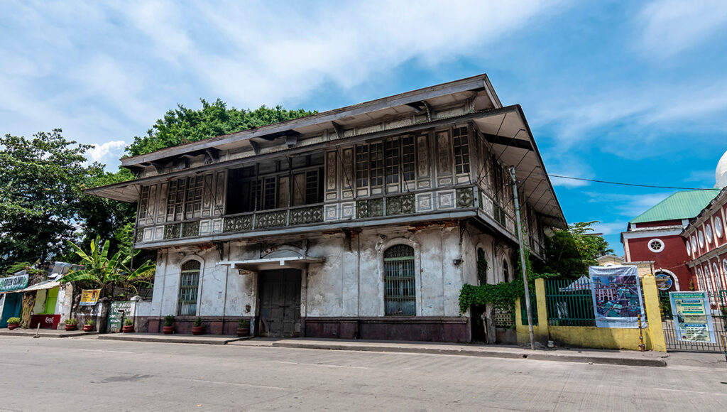 A grand Spanish-colonial era heritage house with intricate wooden windows and a stone ground floor, reflecting the rich history and architectural heritage that are top things to do in Iloilo City.