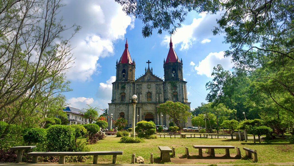 A front-view shot of the historic Gothic-Renaissance Molo Church (Saint Anne Parish) with its distinct red spires and stone facade, seen from the lush Molo Plaza—a must-visit for travelers exploring things to do in Iloilo City.