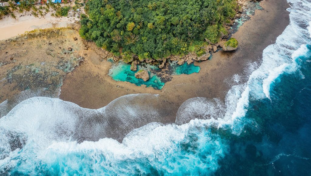 Top-down drone shot of Magpupungko Rock Pools showing vibrant turquoise natural tide pools nestled against a rocky shoreline and dense jungle.