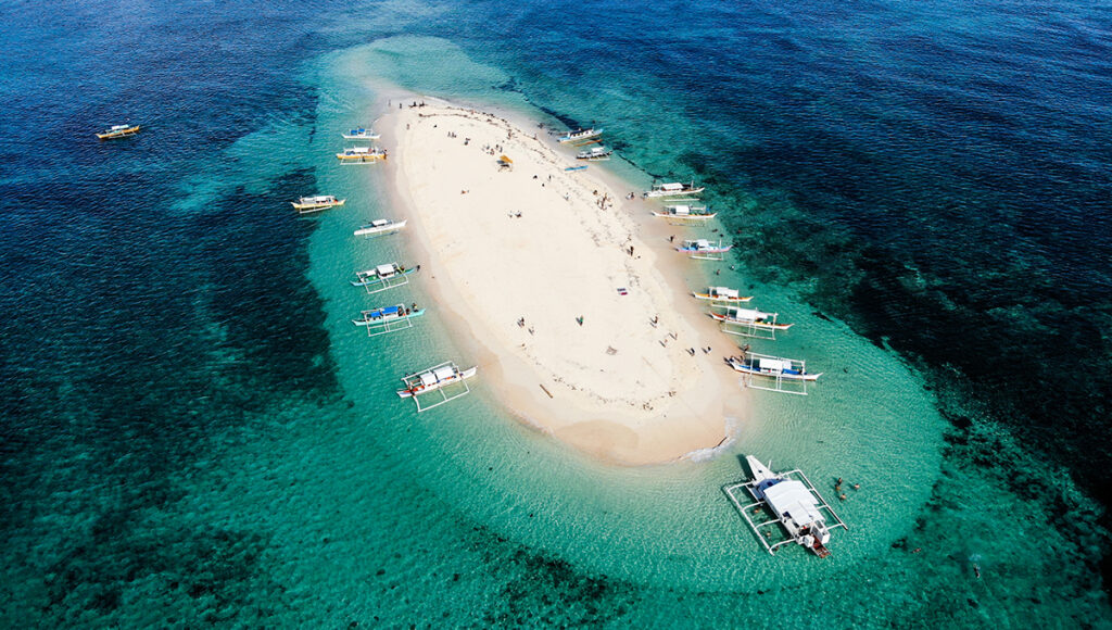 High-angle shot of Naked Island, a pristine white sandbar in Siargao surrounded by crystal clear ocean and tourist boats.