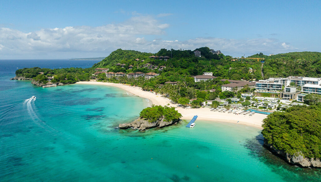 High-altitude drone shot of Boracay's White Beach, showcasing the vibrant blue water and lush palms during the peak dry Philippines