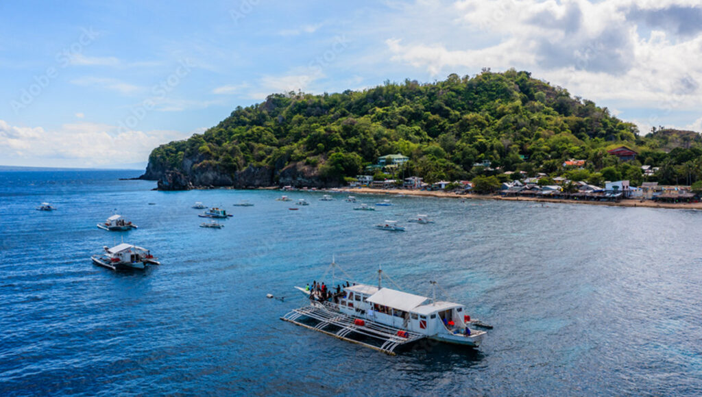 A traditional Filipino outrigger boat (bangka) carrying passengers near a lush coastline, illustrating maritime things to do in Dumaguete.