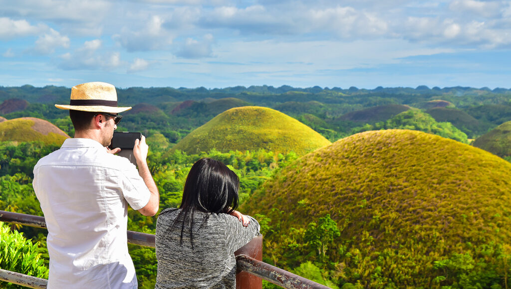 Tourists at a viewpoint overlooking the lush green Chocolate Hills in Bohol, a popular destination during the sunny intervals of Philippines weather May.