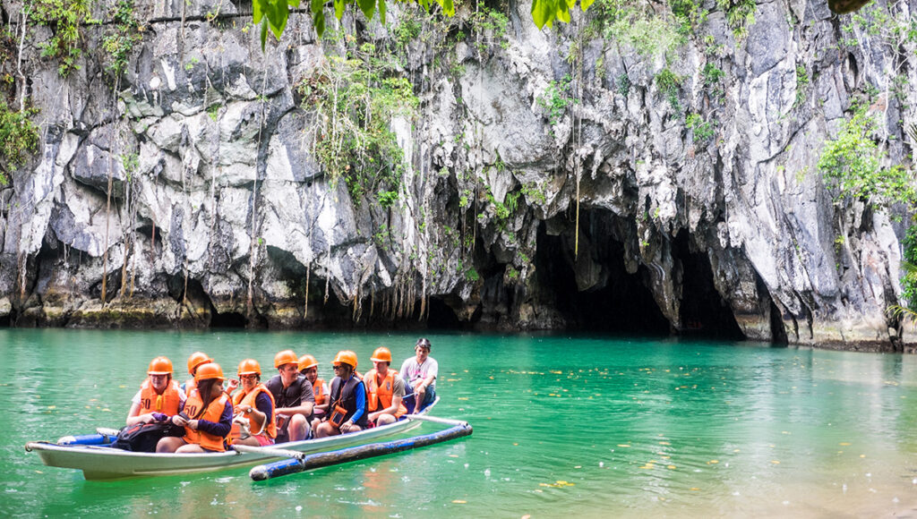 Tourists in life vests exploring a massive sea cave by boat, highlighting the adventurous things to do in Palawan.
