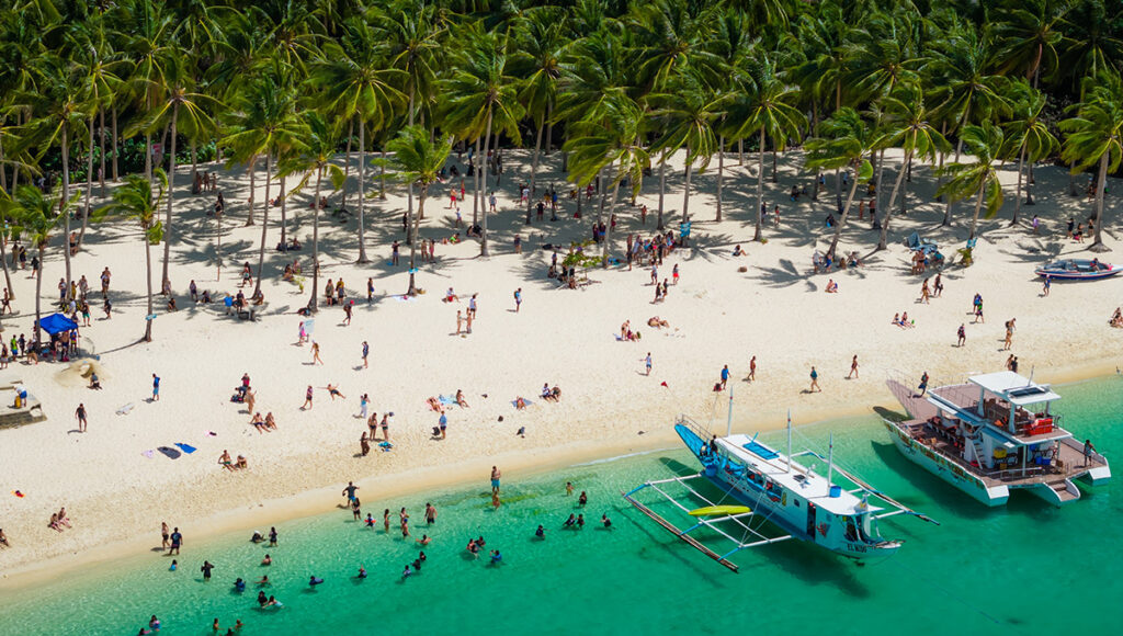 A busy tropical beach with white sand and palm trees, showcasing popular social things to do in Palawan.