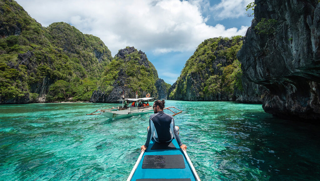 A traveller on a wooden boat entering a turquoise lagoon, a must-see for those looking for things to do in Palawan.