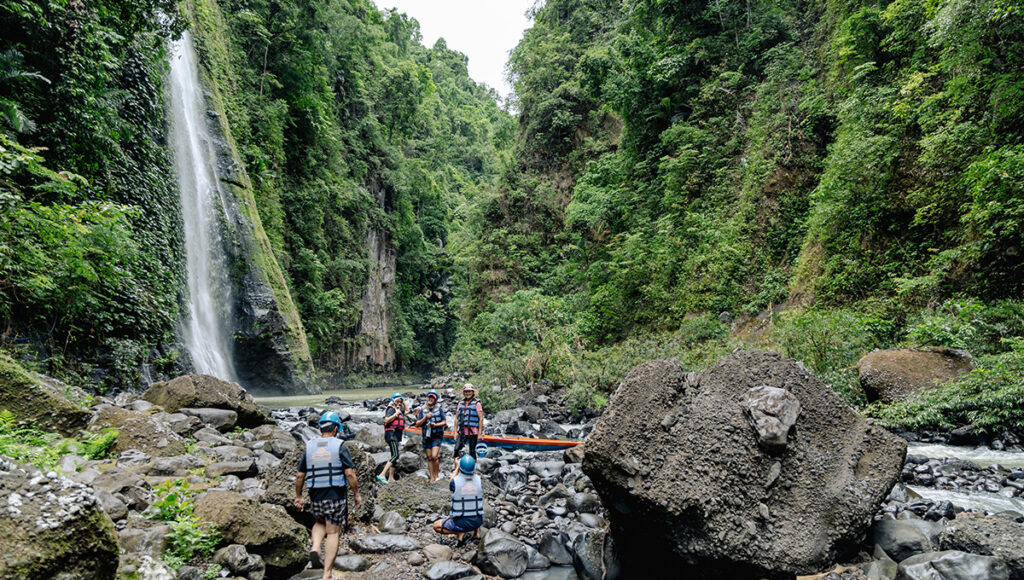 Adventurers wearing life jackets by Pagsanjan Falls in a lush gorge during a river rafting excursion, a highlight of active day trips from Manila.