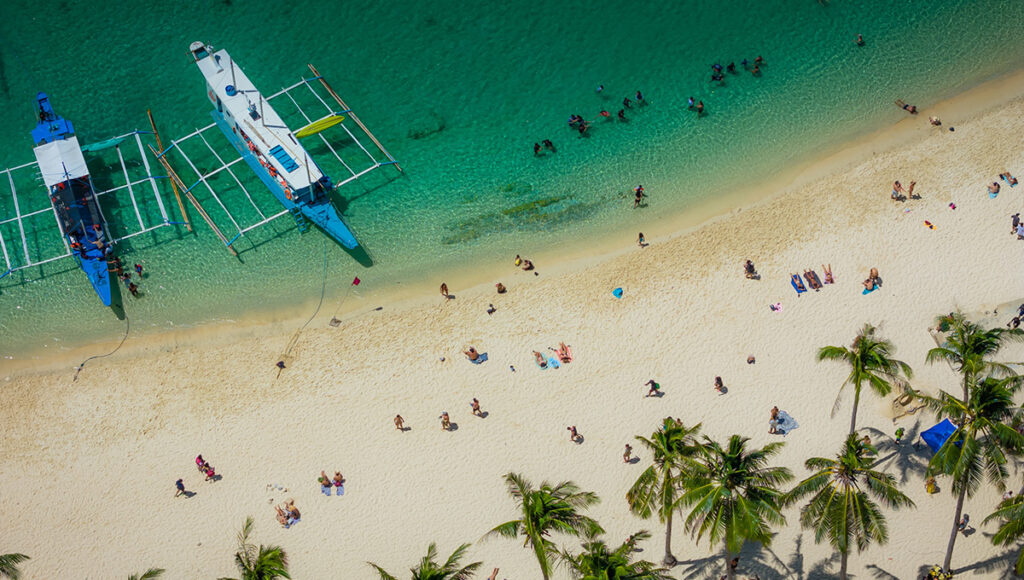 Top-down view of a white sand beach crowded with sunbathers and traditional boats, reflecting the vibrant island life found throughout 2 weeks in Philippines.