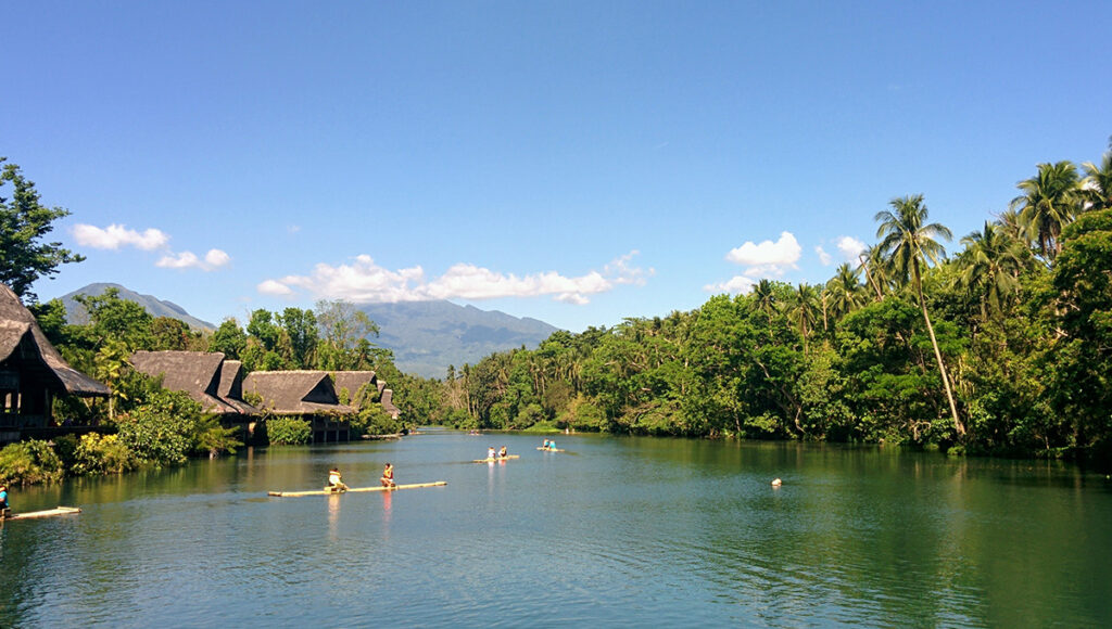 Tourists riding bamboo rafts on a calm tropical river lined with traditional huts at Villa Escudero, a relaxing destination for family day trips from Manila.