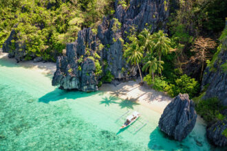 Aerial view of Entalula Island in El Nido, Palawan, with crystal-clear turquoise waters, white sandy beaches, and lush greenery, a breathtaking destination reachable via direct flights to Philippines from UK.