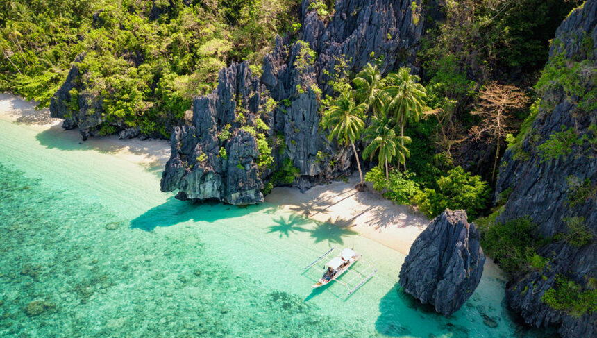 Aerial view of Entalula Island in El Nido, Palawan, with crystal-clear turquoise waters, white sandy beaches, and lush greenery, a breathtaking destination reachable via direct flights to Philippines from UK.
