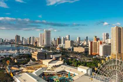 Panoramic view of the modern Manila skyline and waterfront, showing skyscrapers, a marina, and an amusement park with a Ferris wheel in the foreground, suggesting a vibrant and developed city. This image helps answer the question, "Is Manila safe?" by illustrating a bustling, modern urban center.