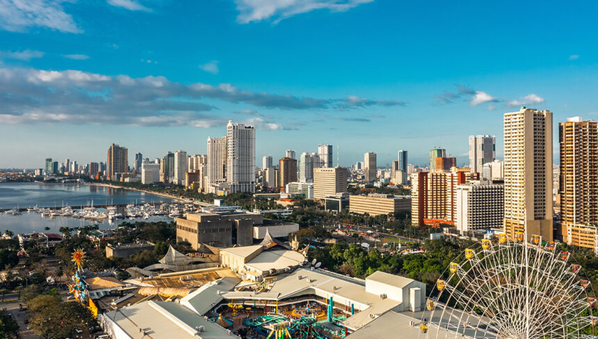 Panoramic view of the modern Manila skyline and waterfront, showing skyscrapers, a marina, and an amusement park with a Ferris wheel in the foreground, suggesting a vibrant and developed city. This image helps answer the question, "Is Manila safe?" by illustrating a bustling, modern urban center.