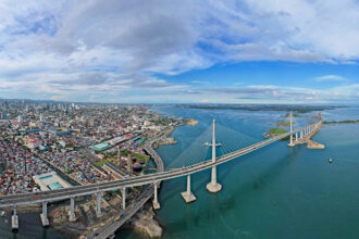 Aerial panoramic view of the massive Cebu City skyline, modern cable-stayed bridge, and harbor, showing the urban side of where to stay in Cebu.