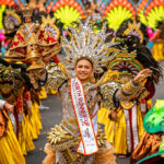 Image of Cebu City Sinulog Festival Queen holding the Santo Niño during the street dance competition, wearing an elaborate gold costume and headdress with crowds in the background.
