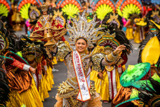 Image of Cebu City Sinulog Festival Queen holding the Santo Niño during the street dance competition, wearing an elaborate gold costume and headdress with crowds in the background.