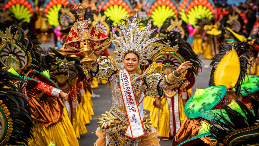 Image of Cebu City Sinulog Festival Queen holding the Santo Niño during the street dance competition, wearing an elaborate gold costume and headdress with crowds in the background.